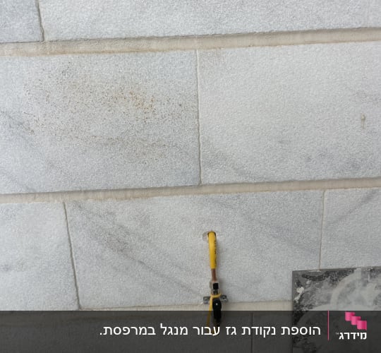 שסתום גז צהוב מותקן על קיר לבנים אפור